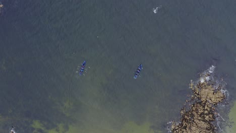 Drohnenperspektive-Von-Oben-Nach-Unten:-Currach-Boote-Kämpfen-Gegen-Die-Strömung,-Um-Aufs-Meer-Hinauszurudern