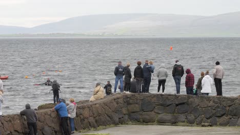 Spectators-stand-at-watch-cheering-for-boat-racers-in-currachs,-ireland