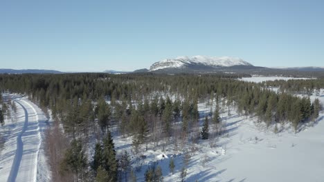 Drohnenaufnahme,-Die-Nach-Oben-Fliegt-Und-Gefrorene-Seen,-Eine-Straße,-Wälder-Und-Schnee-Mit-Einem-Berg-Im-Hintergrund-In-Nordschweden-Zeigt