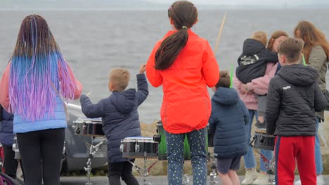 Rear-view-of-children-hopping-dancing-hitting-and-playing-drums-by-the-beach-on-chilly-day