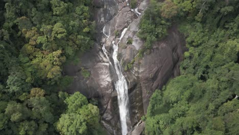 Smooth-slow-aerial-tilt-up-granite-wall-Air-Terjun-Waterfall,-Malaysia