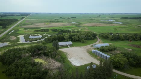 Cinematic-Aerial-Drone-Orbit-Around-Western-Canada-Pasture-Countryside-Agriculture-Demonstration-Cattle-Farm-House-Crop-Bins-and-Nature-Prairie-Field-Landscape-with-Highway-Riparian-Lake