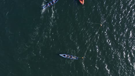 Drone-rises-to-bird's-eye-view-perspective-with-currach-irish-canoe-boats-tethered-to-buoys-in-open-ocean