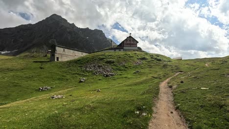 Wandervideo-über-Die-Annäherung-An-Eine-Berghütte-Auf-Einem-Grünen-Hügel-Vor-Hochalpinen-Bergen