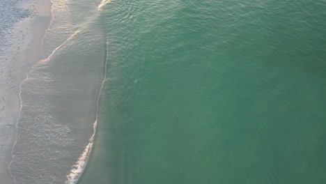 Aerial-view-of-Gulf-of-Mexico-waves-on-Pensacola,-Florida-Beach-pan-up-to-the-sunrise-and-fluffy-clouds