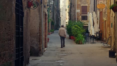 Anciano-Está-Caminando-Por-La-Calle-Estrecha-Del-Pueblo-Medieval-De-Pitigliano-En-Toscana,-Italia