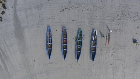 Static-bird's-eye-view-of-currach-boats-on-sandy-beach-as-workers-separate-oars