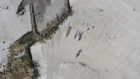 Rotating-drone-above-ladies-beach-galway-ireland-as-people-walk-currach-boats-closer-to-waters-edge