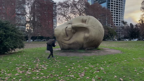 A-stable-shot-of-a-tourist,-who-photographs-a-head-sculpture-in-the-park