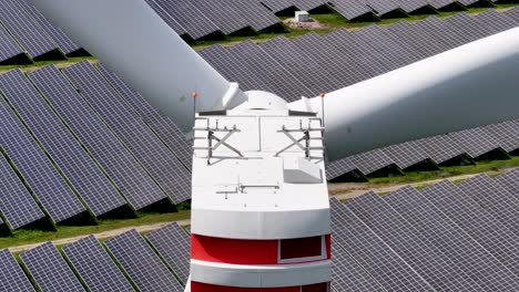 Eine-Windkraftanlage,-Die-In-Einem-Solarpark-Saubere-Energie-Erzeugt-–-Reihen-Von-Solarpaneelen-Hinter-Den-Sich-Drehenden-Rotorblättern-–-Starker-Parallaxeneffekt-–-Langes-Teleobjektiv