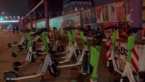 Many-electric-Lime-green-Scooter-parked-in-Berlin-city-at-night,-wide-shot