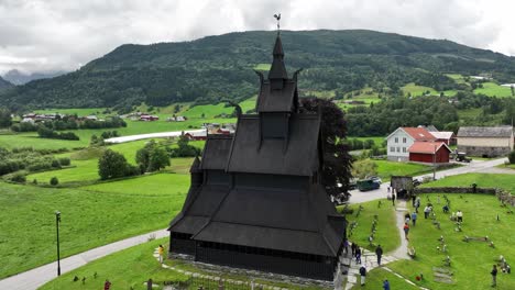 Tourists-exit-historic-Hopperstad-Stave-Church-at-Vik-in-Sogn-Norway---Full-orbit-aerial-at-different-heights-with-people-walking-outside