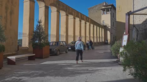 Una-Mujer-Camina-Por-La-Ciudad-Medieval-Con-Un-Muro-Arqueado-En-Pitigliano,-Toscana,-Italia