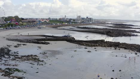 Drone-rises-above-low-tide-water-line-at-ladies-beach,-reveals-galway-ireland-coast-and-salthill-promenade