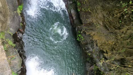 Young-adult-Man-cliff-jumping-off-a-high-tombstoning-Platform-at-Kembar-Waterfall-of-Aling-Aling-Trek-amid-lush-tropical-jungle,-Bali