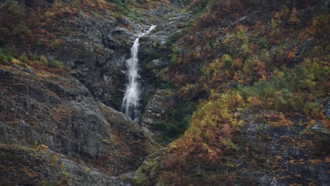 Wunderschöner-Wasserfall,-Eingerahmt-In-Einer-Felsigen-Berglandschaft-Mit-Herbstlichen-Roten-Und-Gelben-Bäumen