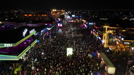 Aerial-view-over-people-and-colorful-lights-at-the-San-Marcos-fair,-night-in-Aguascalientes,-Mexico