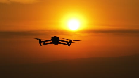 Silhouette-drone-rising-with-a-vibrant-orange-sunset-sky-background-with-clouds