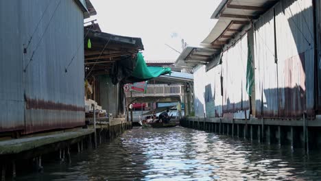 Zooming-in-to-a-wooden-boat-that-is-cruising-in-the-canal-of-Damoen-Saduak-Floating-Market,-Thailand