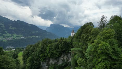 Kirchenglockenturm-Mit-Turmspitze,-Geschmückt-Mit-Wunderschöner-Natur-Der-Schweiz,-Aufgenommen-Von-Einer-Drohne