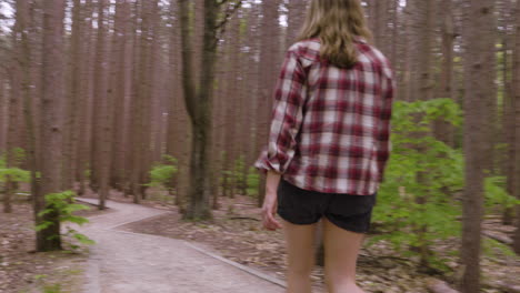 Sweeping-handheld-shot-of-a-young-woman-walking-along-a-path-in-the-woods