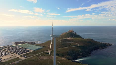 Wind-Turbine-Near-The-Sea-Farm-With-Cape-Villano-Lighthouse-And-Museum-In-The-Background-In-Camariñas,-A-Coruña,-Spain