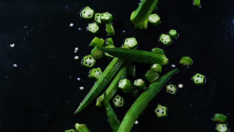 Cinematic-slow-motion-footage-of-okra-or-lady's-fingers-being-tossed-on-a-dark-and-wet-working-surface,-partly-cut-and-partly-full