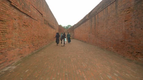 Indian-tourists-wearing-ethnic-clothes-enter-through-a-narrow-lane-of-brick-mason-work-on-the-site-of-Nalanda-Mahavihara-an-ancient-Buddhist-monastic-university-that-was-ruined-by-Mughal-Invaders