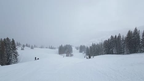 Handheld-landscape-shot-during-a-cold-windy-snowstorm-from-the-top-of-a-run-in-a-beautiful-ski-resort-in-the-Rocky-Mountains-of-Utah-surrounded-by-pine-trees-on-a-overcast-winter-day
