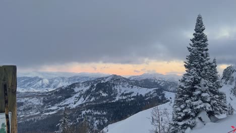 Handheld-shot-of-a-stunning-winter-landscape-scene-looking-down-at-a-cloudy-snow-covered-valley-during-a-golden-sunset-from-the-summit-of-a-ski-resort-in-the-Rocky-Mountains-of-Utah