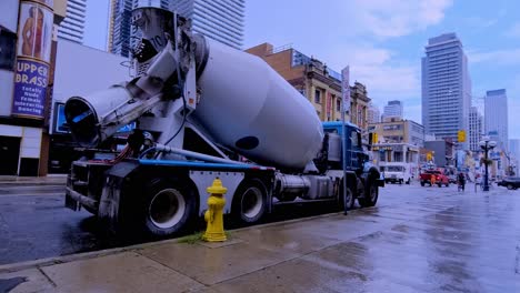 Downtown-Toronto-concrete-mixing-truck-parked-on-Yonge-Street-in-front-of-a-yellow-fire-hydrant-one-after-the-other-as-the-city-morphs-to-a-post-modern-futuristic-architectural-marvel-of-advancement