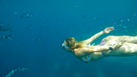 Young-blonde-female-swimmer-with-dive-mask-chasing-little-fish,-slow-motion
