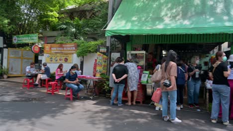 Panning-from-the-left-side-of-the-street-to-the-right-side-of-the-street,-you-can-see-people-eating-on-the-side-while-others-are-queueing-for-their-orders-of-the-famous-papaya-salad-and-grilled-meat
