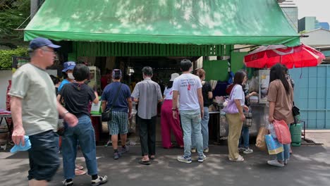 Panning-from-street-on-the-right-side-of-the-frame,-to-the-local-street-restaurant-filled-with-customers-waiting-for-their-orders-of-Somtam-papaya-salad,-grilled-chicken-and-pork