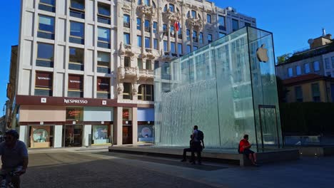 Static-shot-of-tourists-sitting-around-a-water-fountain-at-Apple-Liberty-Square-in-Milan,-Italy-during-morning-time