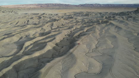 Drohnen-Luftaufnahme-Eines-Roten-Fahrzeugs-Auf-Einer-Unbefestigten-Straße-Und-Einem-Sandsteinhügel-In-Der-Weite-Der-Wüste-Von-Utah,-USA