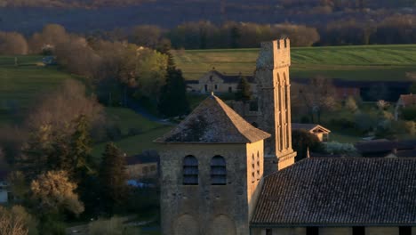 Aerial-view-of-a-church-in-France-using-a-telephoto-lens,-drone-shot-of-the-steeple-with-a-circular-movement,-pigeons-flying-around-the-steeple,-Saint-Avit-Sénieur-in-the-Dordogne