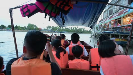 Taking-pictures-and-videos-while-on-a-boat-ride,-a-group-of-tourists-are-happily-sightseeing-as-they-are-cruising-along-the-canals-of-Amphawa-Floating-Market-in-Thailand