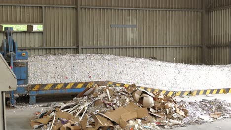 Bales-of-shredded-paper-exiting-baler,-moving-on-conveyor-in-recycling-center