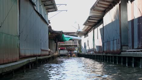 The-boatman-is-maneuvering-the-wooden-boat-with-a-group-of-tourists-in-the-canal-of-the-popular-tourist-destination-in-Thailand,-the-Damnoen-Saduak-Floating-Market