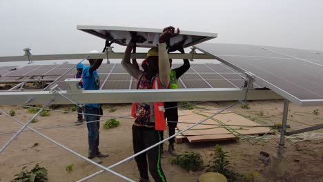 Static-handheld-shot-of-african-construction-workers-wearing-hard-hats-while-building-photovoltaic-panels-for-sustainable-power-and-environmental-protection-in-gambia-in-west-africa