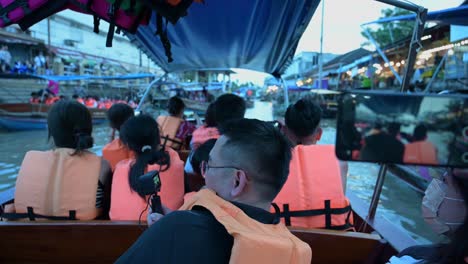 Los-Grupos-De-Turistas-Que-Toman-Un-Paseo-En-Bote-En-El-Mercado-Flotante-De-Amphawa-Están-Ocupados-Tomando-Fotografías-Y-Videos-Mientras-Hacen-Turismo,-Mientras-Pasan-Por-Restaurantes-Y-Tiendas-De-Souvenirs-A-Lo-Largo-De-Los-Lados-Del-Canal.