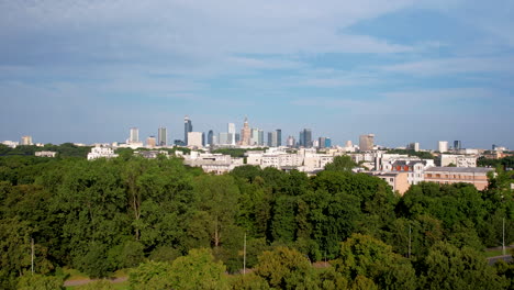 Drone-shot-over-green-trees-from-left-to-right---In-the-distance,-a-panorama-of-Warsaw-with-visible-skyscrapers-and-the-Palace-of-Culture-in-the-city-center