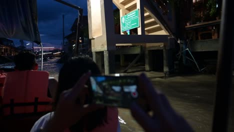 Tourists-taking-videos-of-the-restaurants-and-souvenir-shops-along-the-canals-of-Amphawa-Floating-Market-in-Thailand