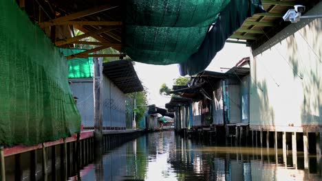 Se-Pueden-Ver-Tiendas-De-Souvenirs-Cerradas-A-Los-Lados-Del-Mercado-Flotante-Damnoen-Saduak-En-Tailandia,-Mientras-Los-Turistas-Toman-Un-Lento-Y-Tranquilo-Paseo-En-Bote.