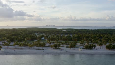 Rising-aerial-drone-shot-of-the-beautiful-tropical-beach-surrounded-by-palm-trees-on-Crandon-Park-in-Key-Biscayne-outside-of-Miami,-Florida-on-a-warm-sunny-summer-evening