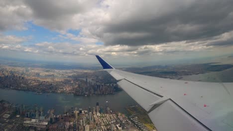 Plane-Window-View-Flying-Over-Jersey-City-with-Manhattan,-Brooklyn,-and-Queens-in-the-Background-in-the-Afternoon