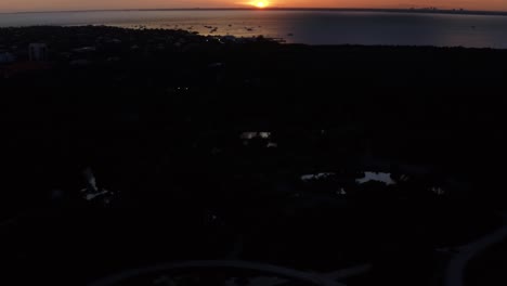 Right-trucking-tilt-up-aerial-drone-shot-revealing-a-orange-golden-ocean-sunset-with-tropical-greenery-below-from-Crandon-Park-in-Key-Biscayne-outside-of-Miami,-Florida-on-a-warm-sunny-summer-evening