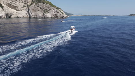 Toma-De-Drone-De-Un-Barco-A-Motor-Navegando-En-El-Mar-Jónico-Azul-Por-La-Costa-De-La-Isla-De-Zakynthos,-Grecia