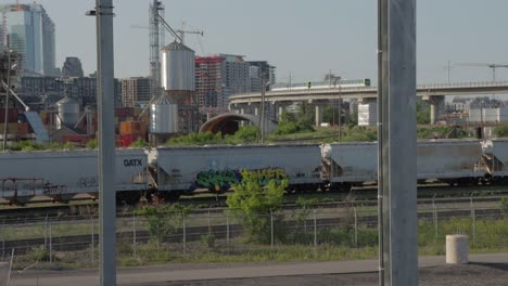 Montreal-Réseau-Express-Métropolitain-Rem-Tren-Circulando-Por-Una-Línea-Elevada-Frente-Al-Horizonte-Y-Trenes-De-Carga-Detenidos-Durante-La-Hora-Dorada